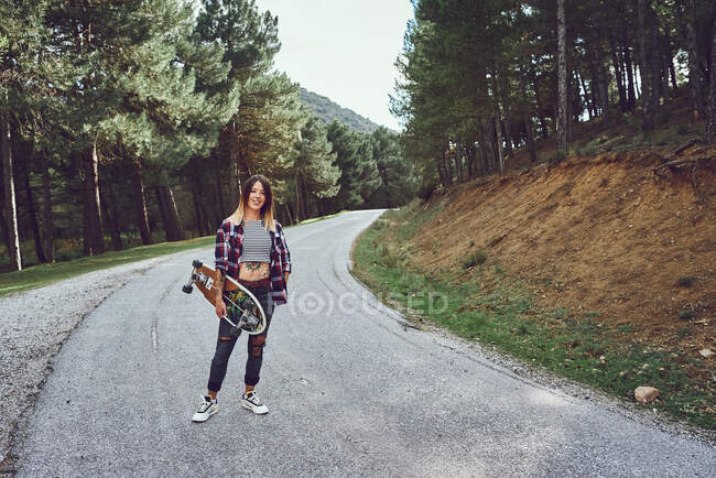Uma mulher com um skate em uma estrada de montanha — Fotografia de Stock