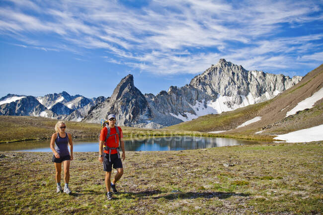 Coppia zaino in spalla in pittoresco prato alpino, montagne dietro. — Foto stock