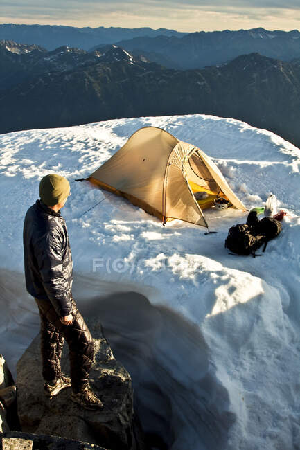 Homem em pé no cume da montanha, olhando para a tenda e vista panorâmica — Fotografia de Stock