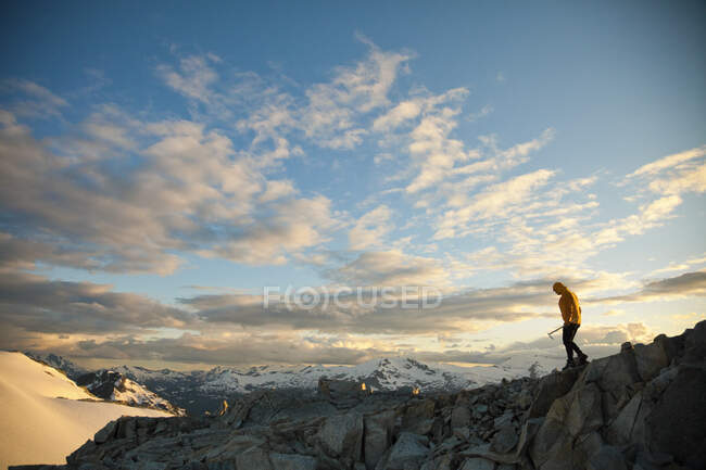 Mountaineer holding ice axe navigates a rocky mountain ridge. — Stock Photo