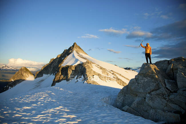 Successful climber wearing yellow jacket stands on rocky outcrop. — Stock Photo