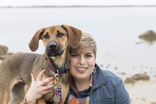 Portrait of a smiling short-haired woman with her brown puppy at beach — Stock Photo