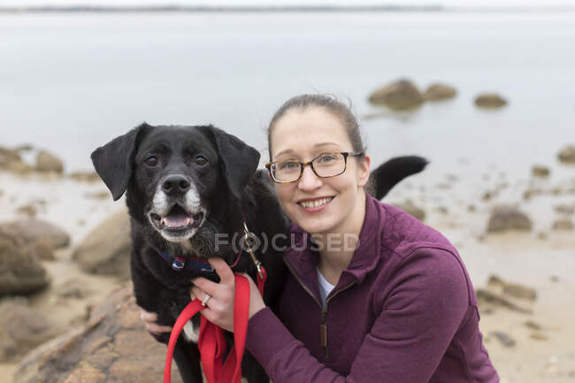 Close-up portrait smiling woman with old black lab at Cape Cod beach — Stock Photo