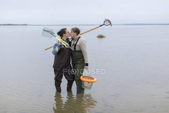 Mesmo sexo casal feminino em waders beijando e de pé no oceano — Fotografia de Stock