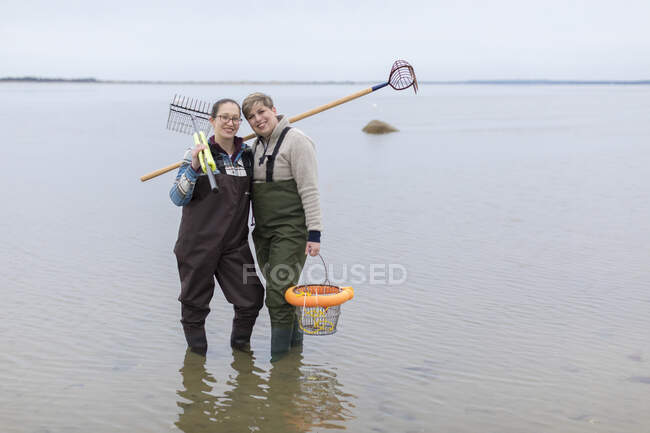 Retrato do casal feminino do mesmo sexo em waders em pé no oceano — Fotografia de Stock