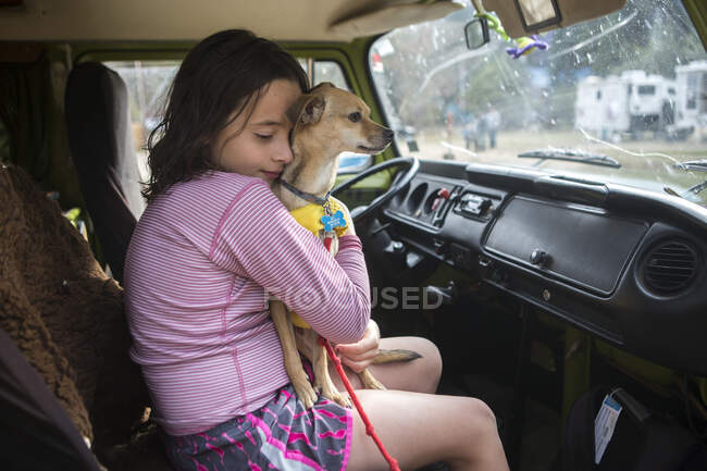 Una chica abraza a un perro chihuahua en VW caravana durante el viaje en carretera - foto de stock