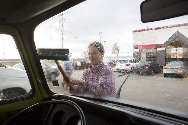 A woman cleans the windshield of VW camper van during roadtrip — Stock Photo