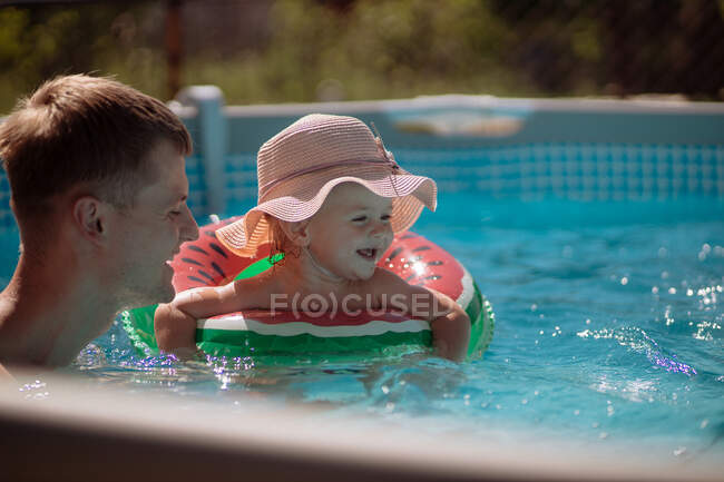 Niña con sombrero nada en la piscina con papá - foto de stock