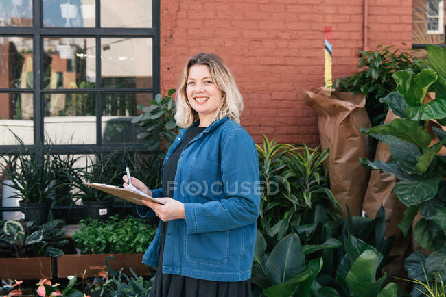 Mujer de negocios sonriente sosteniendo portapapeles de inventario en la pequeña empresa - foto de stock