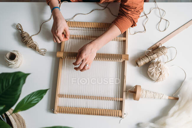 Руки жінки плетуть вовняний килим за столом з квітами і нитками — стокове фото