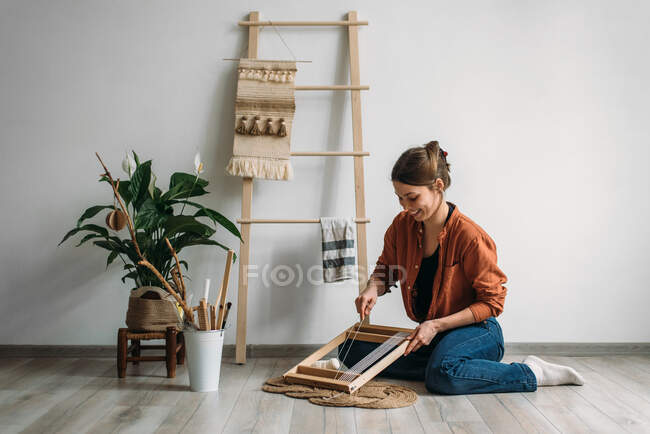 Жінка плете вовняний килим на підлозі перед білою стіною — стокове фото
