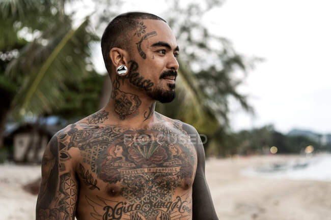 Ragazzo tailandese sulla riva del mare tra le palme tutto in tatuaggi — Foto stock