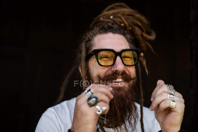 Retrato de um cara hipster com óculos e com dreadlocks e uma tatuagem se senta no fundo de uma casa de madeira — Fotografia de Stock