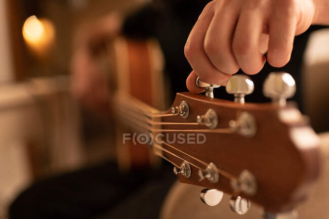 Крупный план обрезанный человек крутит колышки и настраивает гитару во время репетиции в домашней студии — стоковое фото