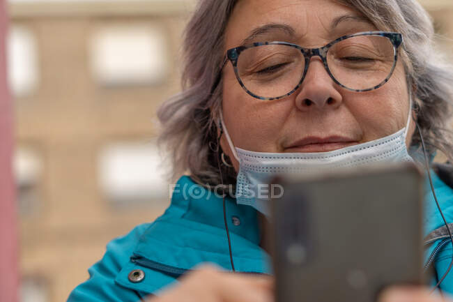 Mujer de pelo blanco bebiendo café en el bar mientras escribe y mira el teléfono - foto de stock