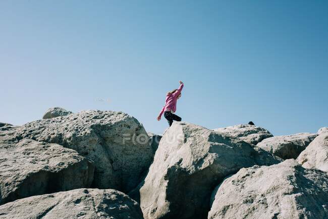 Joven chica corriendo a lo largo de grandes rocas jugando en el sol - foto de stock