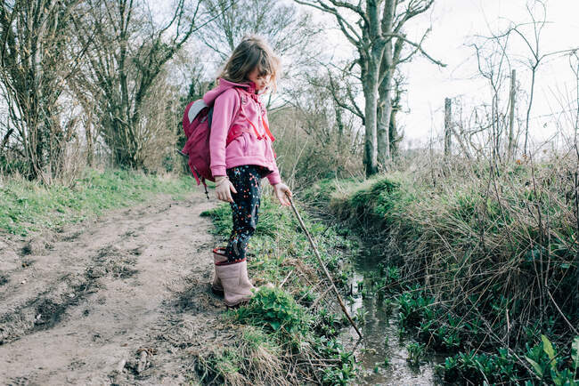 Mädchen spazieren und die Natur mit ihrem Stock in einem Bach erkunden — Stockfoto