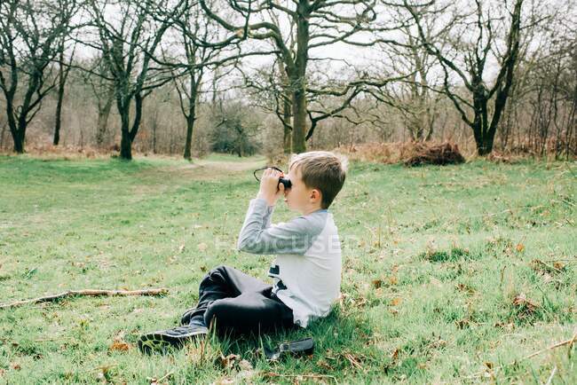 Chico mirando a través de prismáticos en la naturaleza en el campo Inglés - foto de stock