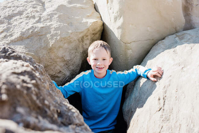 Niño estaba sonriendo en las rocas en la playa en un día soleado en el Reino Unido - foto de stock