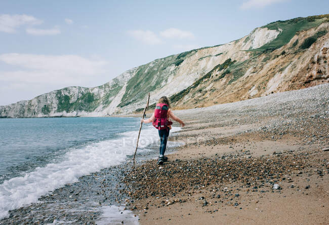 Девушка, идущая вдоль юрского побережья с палкой в прекрасный день — стоковое фото