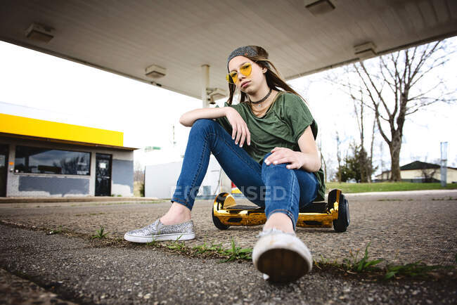 Cool tween girl with blond hair and sunglassess sitting on hoverboard — Stock Photo