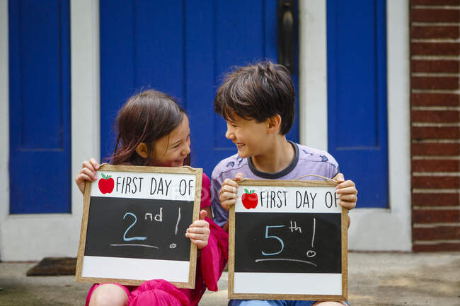 Dos niños felices se sientan juntos en la entrada sosteniendo letreros de Back-to-School - foto de stock