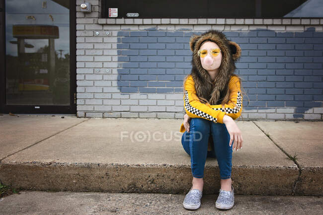 Tween girl sitting on curb with sunglasses and spirit hood. — Stock Photo