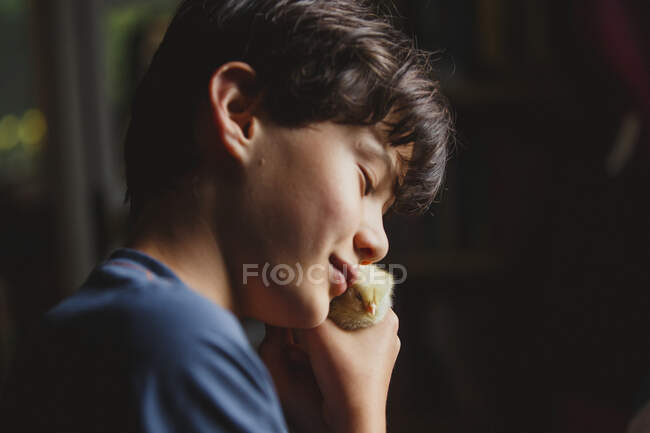 Close-up of happy boy tenderly holding tiny chick up to his face — Stock Photo