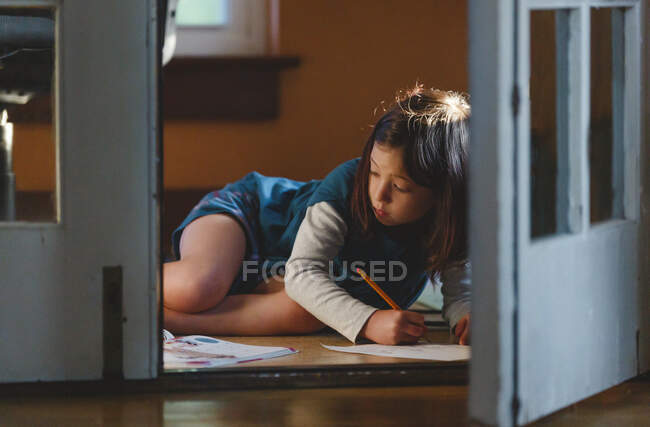 Vista attraverso le porte francesi del bambino che disegna sul pavimento in bella luce — Foto stock