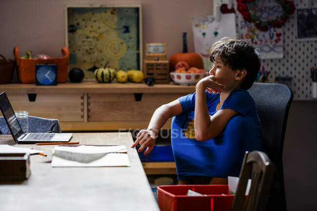 Um menino focado com joelhos dentro da camisa se senta no computador em casa — Fotografia de Stock