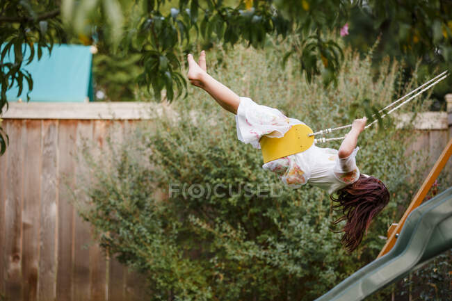 A barefoot child swings high on a playlet in a backyard garden — Stock Photo
