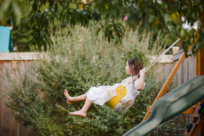 Uma menina descalça feliz balança em um playlet sob uma árvore no verão — Fotografia de Stock