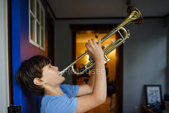 Хлопчик стоїть у барвистому відкритому дверному отворі, граючи трубу — стокове фото