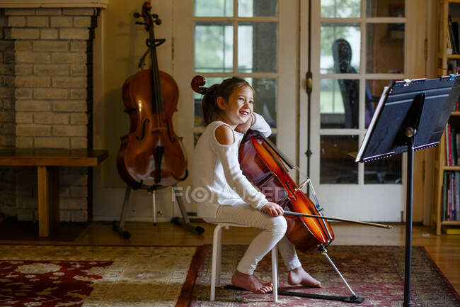 A happy barefoot girl practices her cello in the living room — Stock Photo