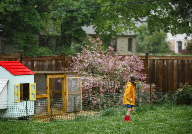 Дитина проходить крізь дощ у яскравому пальто та черевиках на задньому дворі — стокове фото