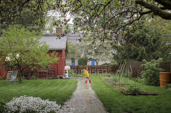 A little girl plays in the pouring rain in backyard garden — Stock Photo