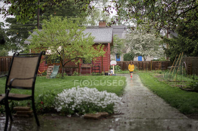 Маленький ребенок идет по тропинке под дождем во дворе сада — стоковое фото
