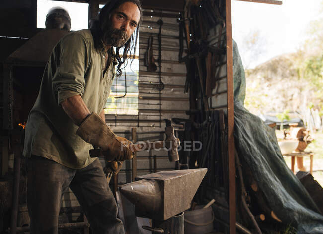 Langhaariger Schmied zeigt Muskatblüte auf Amboss in seiner Werkstatt. — Stockfoto