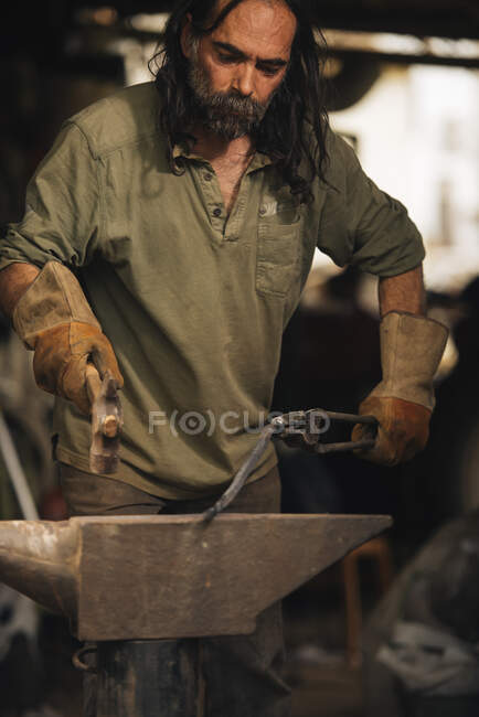 Schmied bearbeitet ein Stück Stahl mit einem Vorschlaghammer auf einem Amboss. — Stockfoto