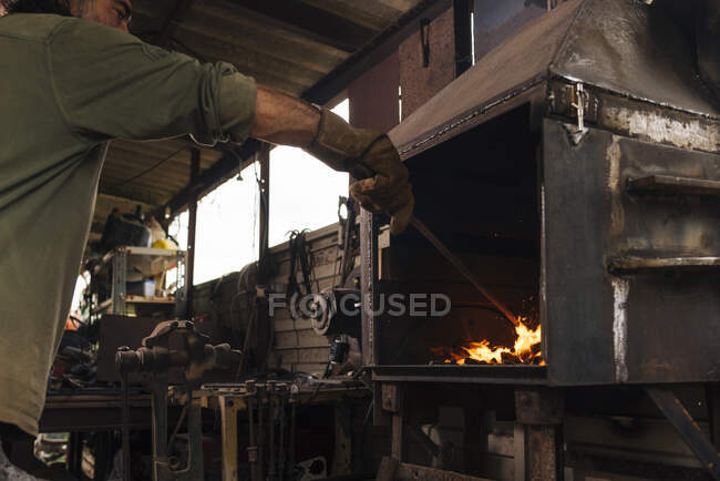 Blacksmith stoking a forge fire in his workshop. — Stock Photo