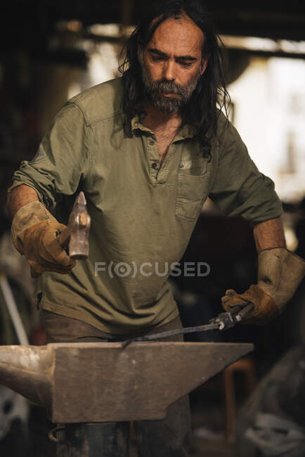 Fabbro che lavora un pezzo di acciaio con una mazza su un'incudine. — Foto stock