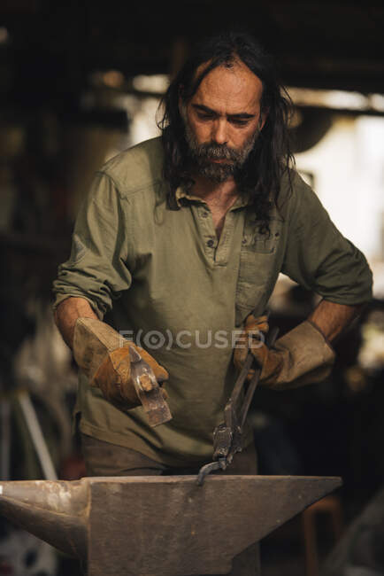 Schmied bearbeitet ein Stück Stahl mit einem Vorschlaghammer auf einem Amboss. — Stockfoto