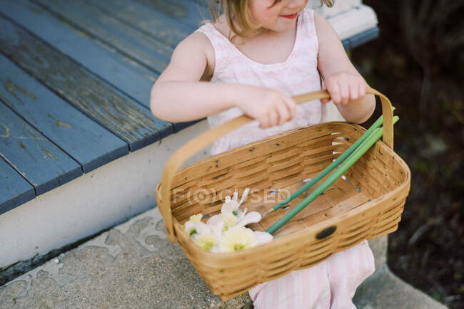 Little girl sitting in a basket with a wooden fence — Stock Photo
