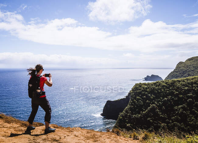 Mujer toma foto del teléfono celular mientras camina cerca del océano en Hawaii - foto de stock