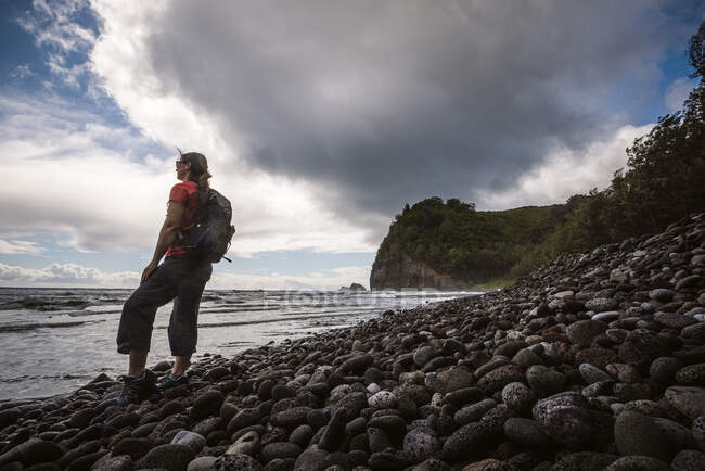 Female hiker with backpack on Pololu Beach, Hawaii looks at Pacific. — Stock Photo