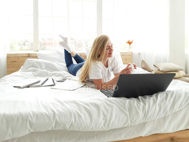 Молода красива жінка працює з ноутбуком у спальні — стокове фото