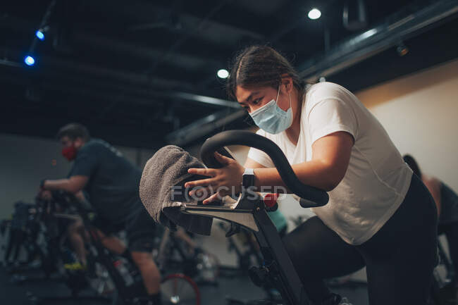 An asian woman pedals on a stationary bike in an indoor bike studio. — Stock Photo