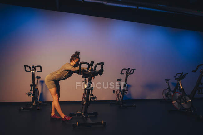 A young Caucasian woman stretches next to a stationary bike. — Stock Photo