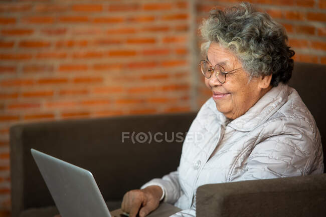 Sonriente mujer mayor ola a cámara que tiene videollamada en el ordenador portátil, - foto de stock
