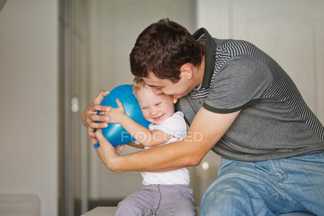 Vater und Sohn lachen und umarmen sich mit blauem Luftballon — Stockfoto
